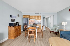 A compact kitchen with wooden cabinets, a refrigerator, and a dining area with a table and chairs.