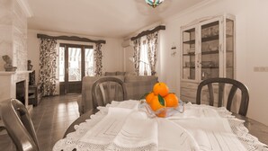 Un comedor con una mesa dispuesta para cuatro, una araña y vistas al salón a través de un vidrio.