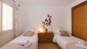 Un dormitorio con dos camas, un aparador de madera, una obra de arte en la pared y un ventanal con cortinas.