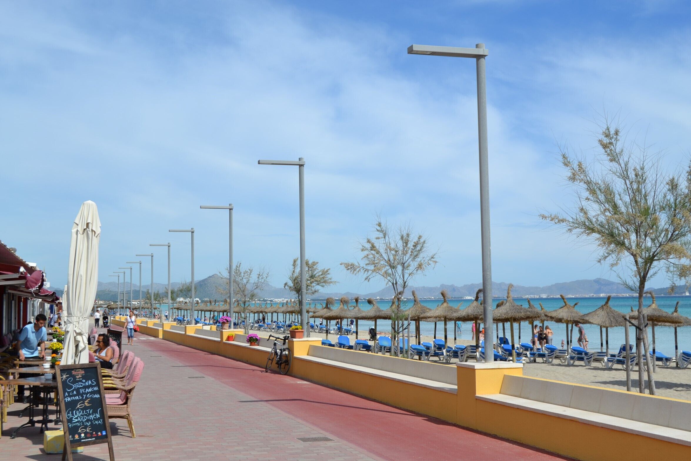 Een boulevard aan zee met terrasjes, parasols en strandstoelen.