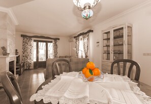 A dining area with a table set for four, a chandelier, and a view of the living room through a glass door.