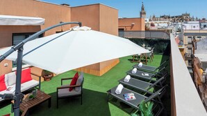 A rooftop terrace with outdoor seating, including a sofa and chairs, and a table with a magazine.