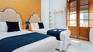 A hotel room with two beds, a nightstand with a lamp, a wooden wardrobe, and a view of the outside.