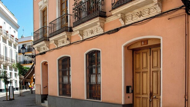 A pink building with ornate balconies, large wooden doors, and a cobblestone street.