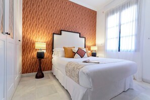 Quarto de hotel bem organizado, com uma cama grande, duas mesas de cabeceira, parede estampada e uma janela com cortinas.