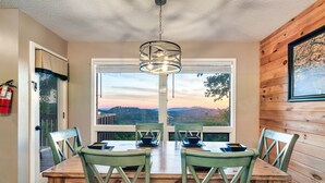 A dining area with a wooden table and chairs, a hanging light fixture, and a view of the outdoors. - Incredible Views! Massage Chairs, Hot-tub, WiFi (Gatlinburg)