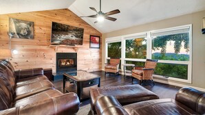 A cozy living room with leather furniture, a fireplace, and large windows offering a view of trees. - Incredible Views! Massage Chairs, Hot-tub, WiFi (Gatlinburg)