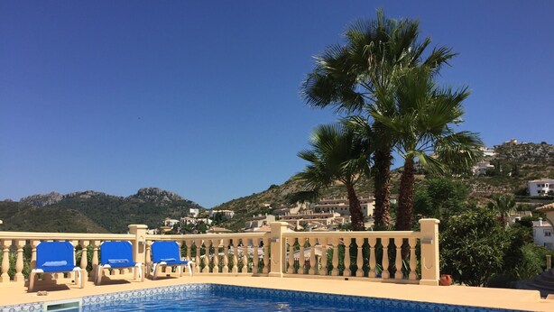 A pool with blue tiles, a white balustrade, and a view of houses on a hillside.
