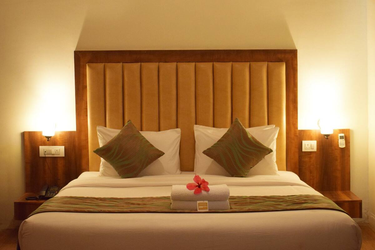 Una cama bien hecha con cabecera de madera, dos lámparas de noche y una mesita con un teléfono.