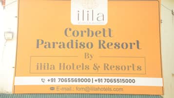 Señal de Corbett Paradiso Resort, un hotel de Ilila Hotels & Resorts, con números de contacto y una dirección de correo electrónico.