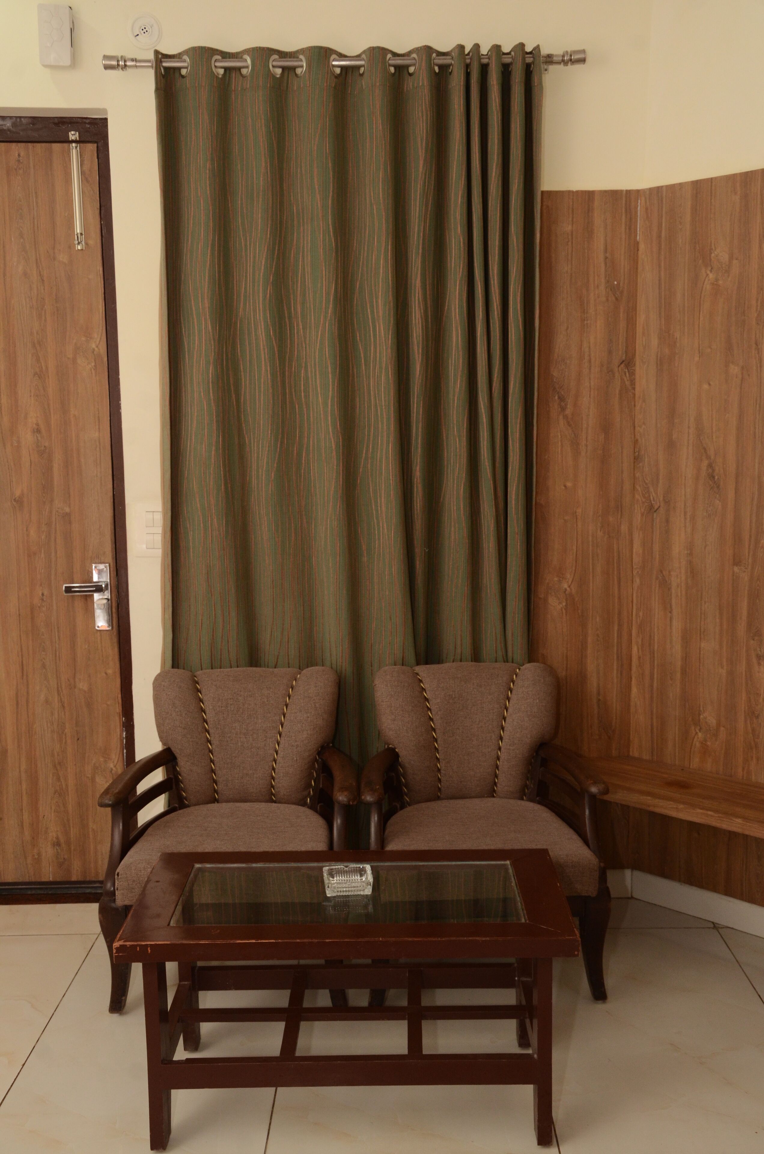 A room with a wooden door, a green striped curtain, two brown armchairs, and a glass-top coffee table.