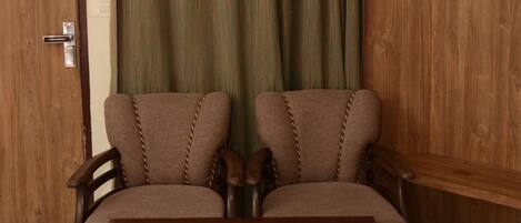 A room with a wooden door, a green striped curtain, two brown armchairs, and a glass-top coffee table.