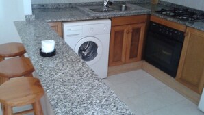 A kitchen with granite countertops, a washing machine, a sink, and a stove. - Residencial Itxaso 8 LEK (Peñiscola)