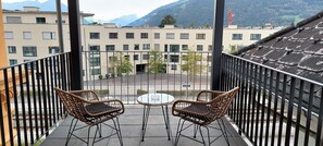 A balcony with wicker chairs and a small table, overlooking a courtyard with buildings and a mountain in the background. - Stylish apartment.  Air-conditioning.  3 mins walk from Interlaken West station. (Interlaken)