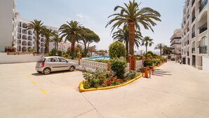A parking area with a car, palm trees, and a pool.