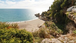 A coastal beach with rocky cliffs and greenery.