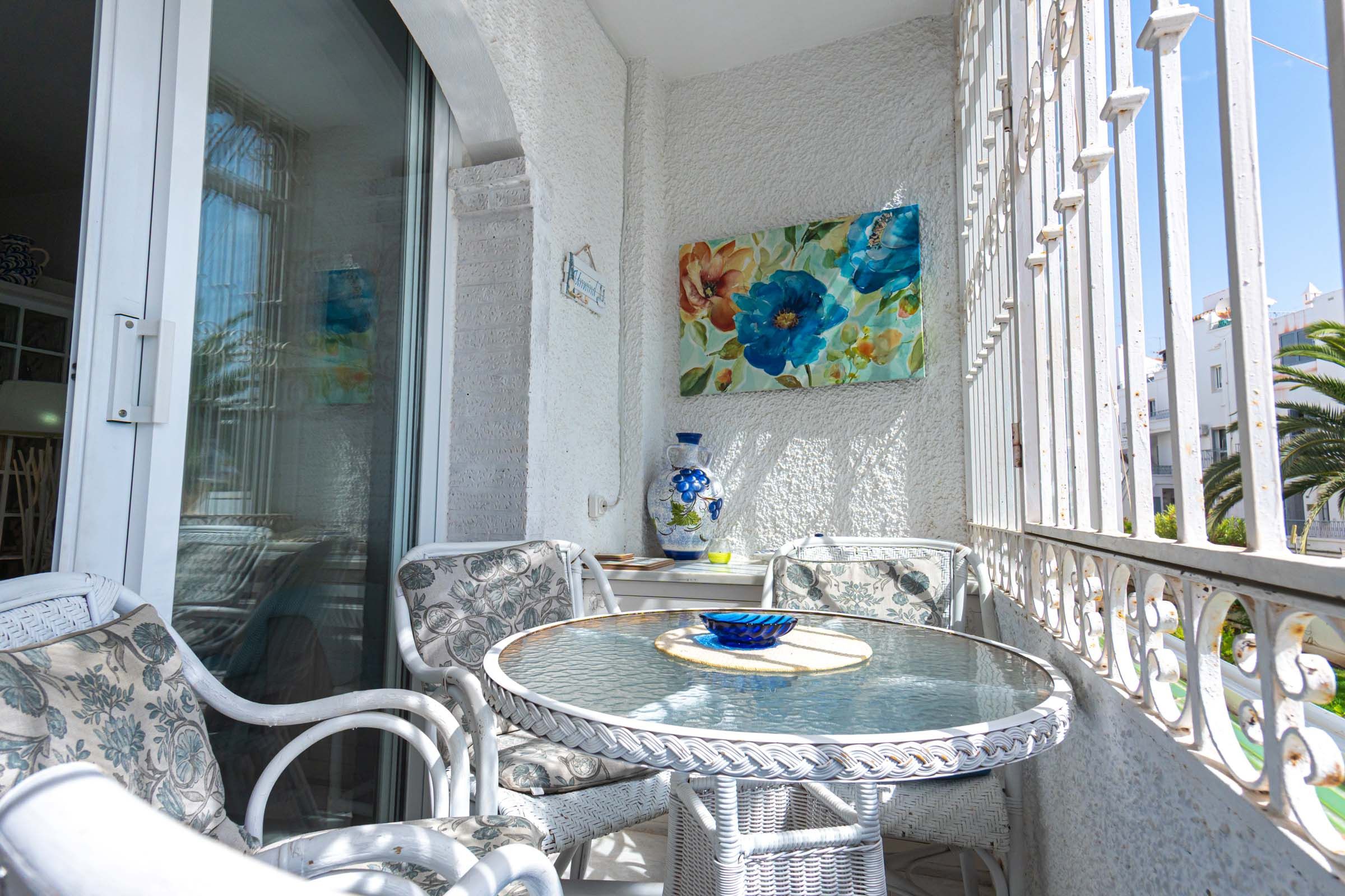 Un balcón con una mesa de vidrio, sillas de mimbre y un jarrón decorativo.