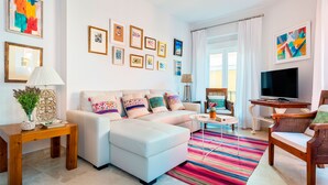 Un salon moderne avec un canapé, un téléviseur, une table basse et un tapis coloré.