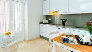 Une cuisine moderne avec des armoires blanches, une hotte en acier inoxydable et un coin repas comprenant une table et des chaises en bois.