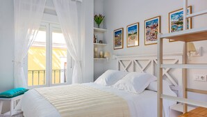 Une chambre à coucher bien rangée, avec un lit, une table de chevet, une fenêtre avec des rideaux et un mur orné de tableaux.