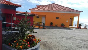 A building with a red and yellow facade, a tiled roof, and a paved ground with potted plants. - Villa E Apartment (Ponta do Sol)