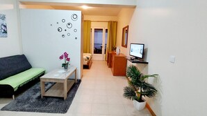 A living room with a sofa, a small table with a plant, a TV, and a potted plant. - Villa E Apartment (Ponta do Sol)