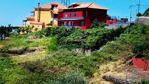 A multi-story building with a red and yellow facade, surrounded by greenery and a hillside. - Villa E Apartment (Ponta do Sol)