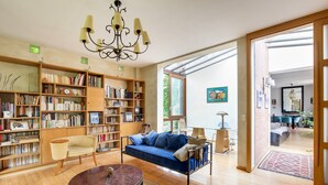 A spacious living room with a sofa, a coffee table, and a bookshelf filled with books. - Superb architect-designed villa in Fontainebleau -1h from Paris (Larchant)