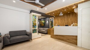A modern reception area with a grey sofa, a wooden reception desk, and colorful artwork on the walls. - RR Residency (New Delhi)