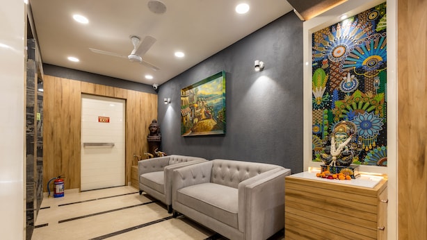A lobby with a reception desk, two sofas, a wooden cabinet, a painting, and an exit sign. - RR Residency (New Delhi)