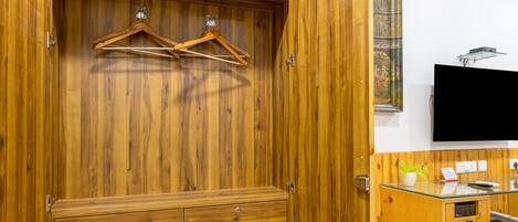 A wooden wardrobe with a mirror, a hanging rack, and a small desk with a chair.