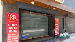 A luxury guest house with a modern facade, large glass doors, and a contact number on a red sign. - RR Residency (New Delhi)