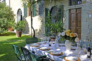An outdoor dining area with a table set for six, surrounded by green chairs, a vase of flowers, and a bottle of wine. - Villa in Cortona with 6 bedrooms sleeps 12 (Cortona)