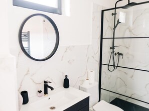 A modern bathroom with a white marble sink, a round mirror, a glass-enclosed shower, and a toilet. - Real Slovakia Experience in the Castle View Village House - live like a local (Krásnohorské Podhradie)