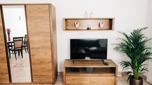 Una sala de estar con un mueble bajo de madera para el televisor, un televisor de pantalla plana, un estante con objetos decorativos, una planta en maceta y un puerta corredera que da a otra habitación.