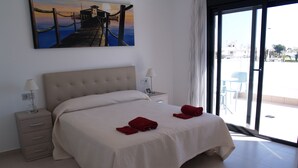 Ein Hotelzimmer mit einem Bett, einem Nachttisch, einer Lampe und einem Gemälde eines Piers.