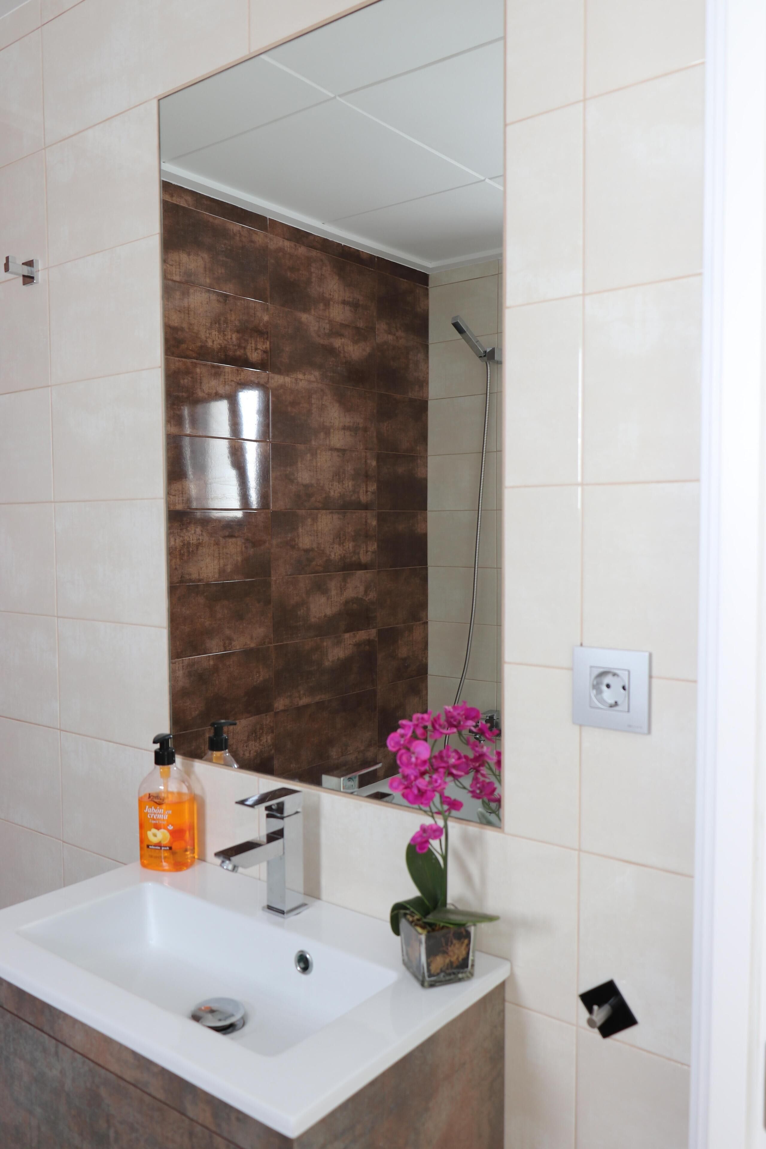 A bathroom with a white sink, a mirror, a shower, and a potted orchid.