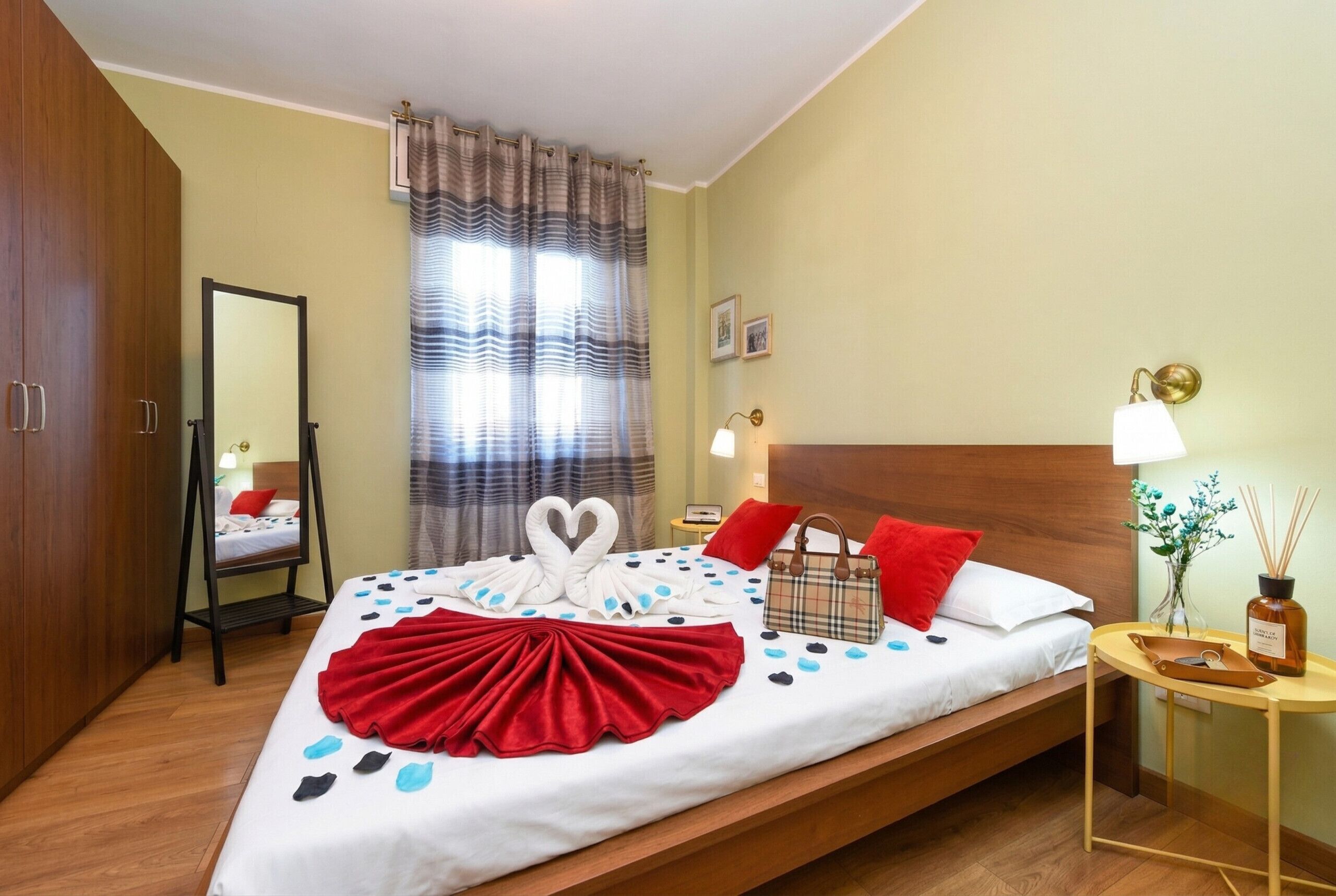 Una camera d'albergo con un letto, un comodino, uno specchio, una finestra con tende e un armadio in legno.