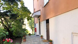 Un sendero empedrado conduce a un edificio de fachada blanca y puerta roja. Hay macetas con flores a lo largo del camino.