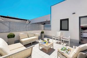 Una terraza en la azotea con mobiliario exterior, una mesa y un ventanal.