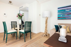 A modern living room with a dining area, featuring a coffee table, chairs, a lamp, and a painting on the wall.