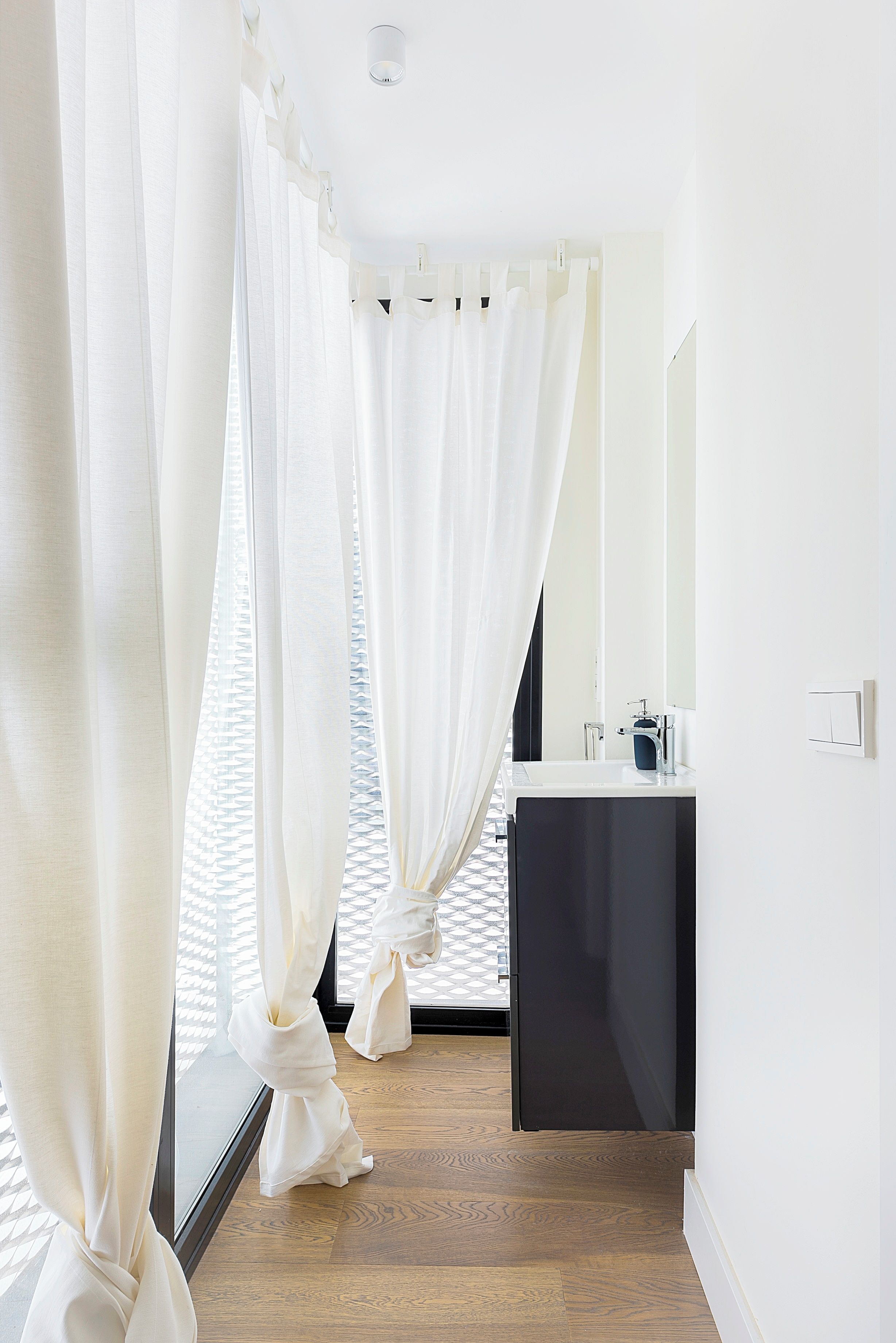 Une salle de bain moderne avec un plancher en bois, un lavabo noir et des rideaux blancs.