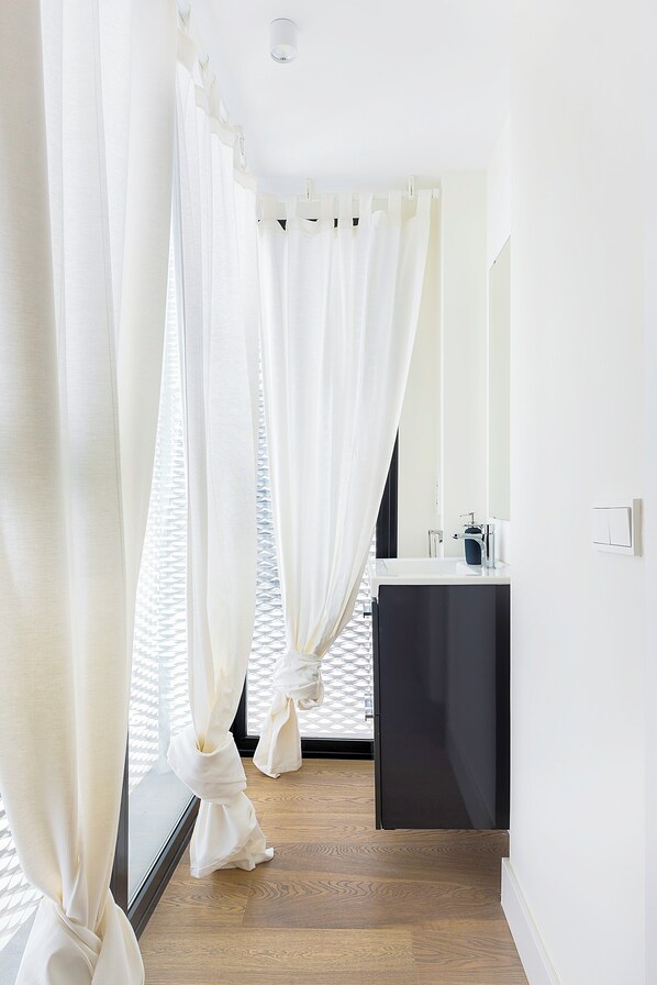A modern bathroom with a wooden floor, a black sink, and white curtains.