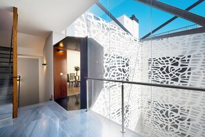 Un interno moderno con una scala, un muro decorato e una zona pranzo visibile attraverso una porta aperta.