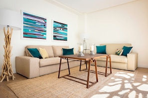 A living room with a beige sofa, a wooden coffee table, abstract paintings, and a floor lamp.