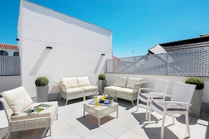Un patio con mobili in vimini bianco, pavimento piastrellato e parete bianca.