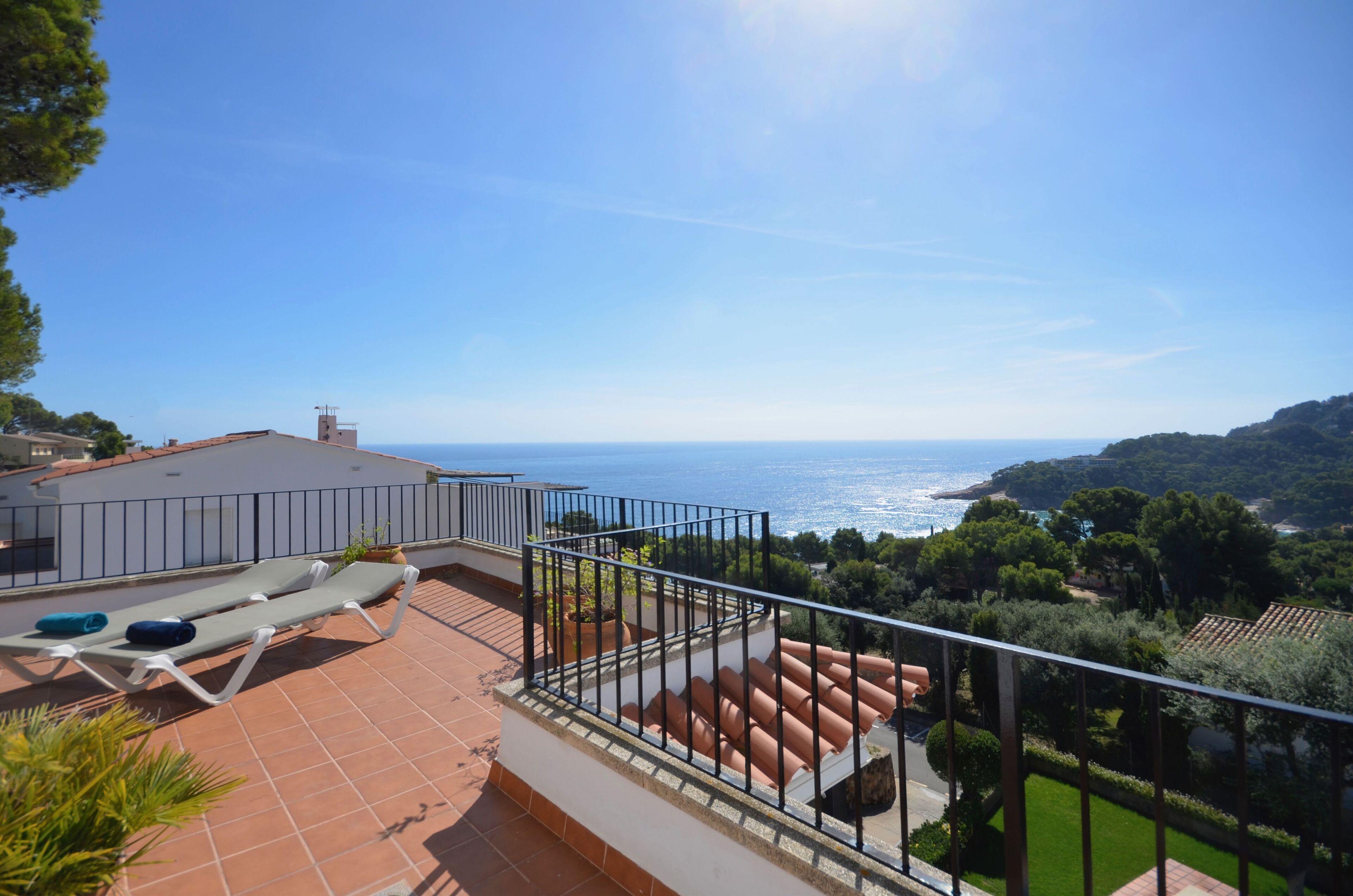 A terrace with a view of the sea, a railing, and a building with a tiled roof.