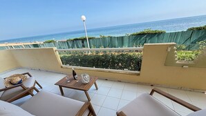 A balcony with a view of the sea, furnished with two wooden chairs and a small table with a bottle and glasses.