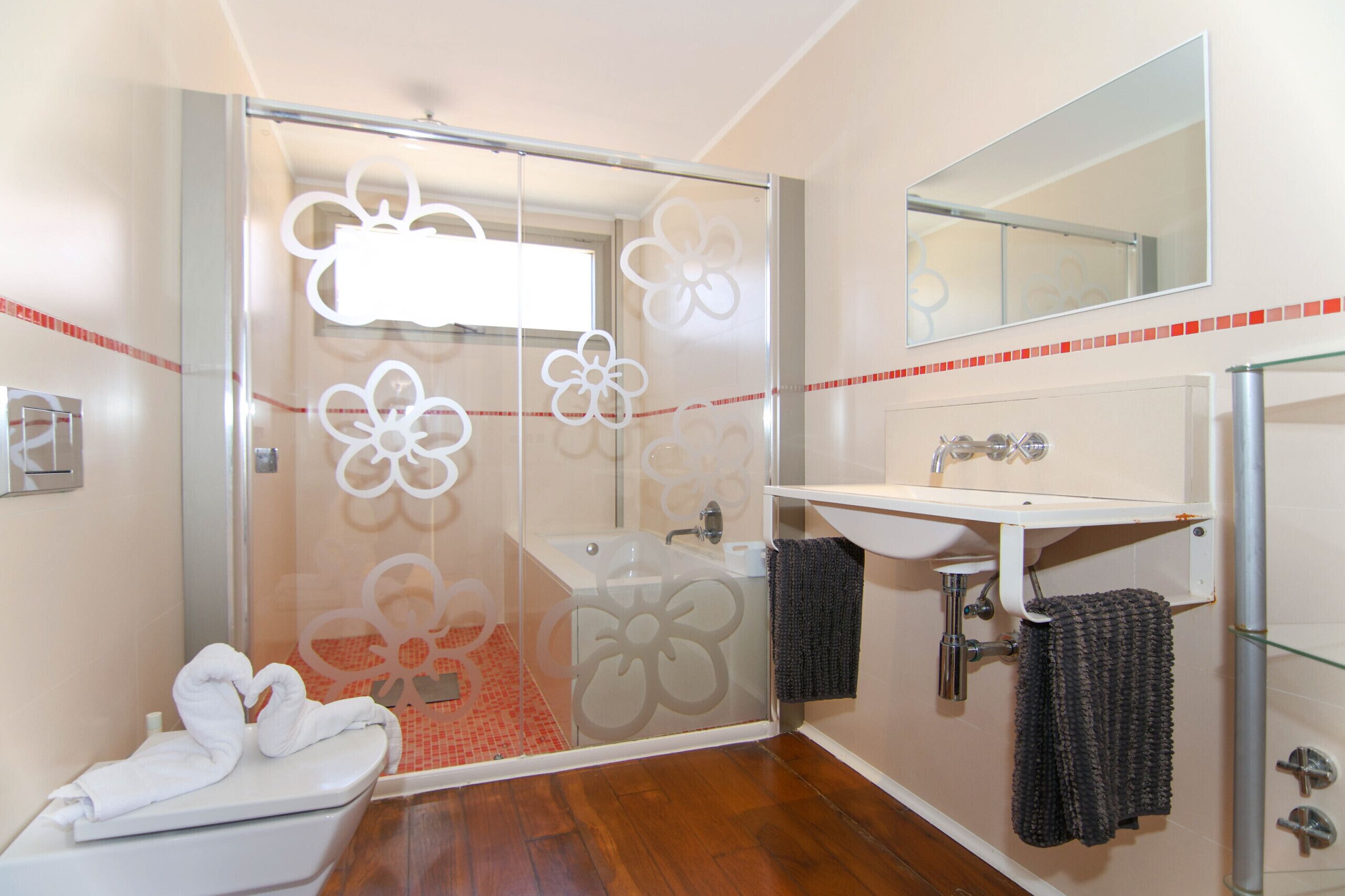 Een badkamer met een douchecabine van glas, een witte wastafel en een toilet.