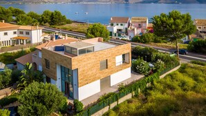 Ett modernt hus med ett platt tak, stora fönster och utsikt över havet och bergen.